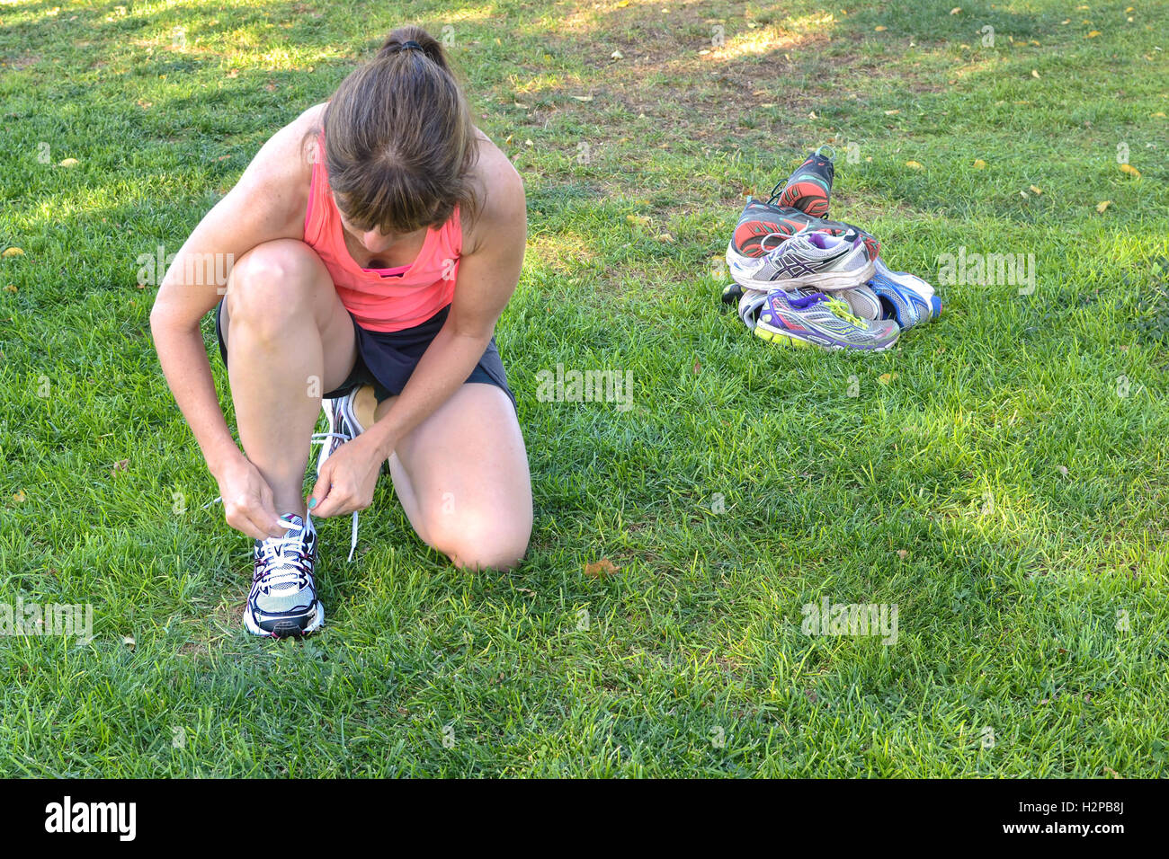 Middle-aged woman tying her running  shoes in front of a pile of old shoes Stock Photo
