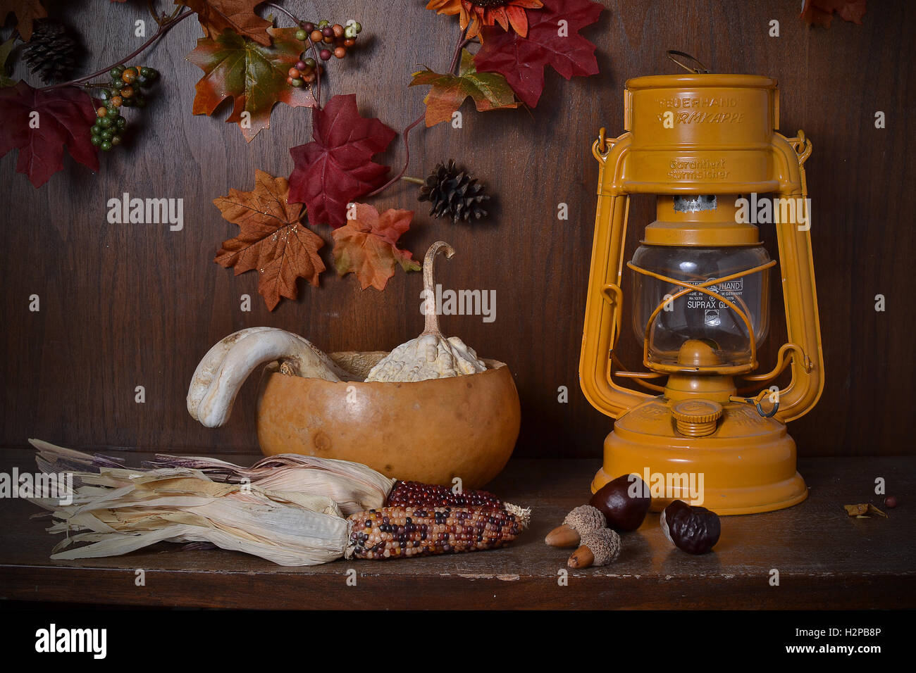 Abstract still life displaying dead, dried harvest symbols and a German gas lantern, against wooden background Stock Photo