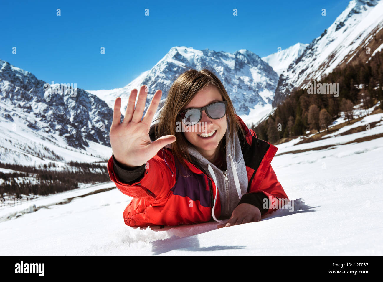 Happy attractive girl lying on the snow on mountains backdrop Stock Photo