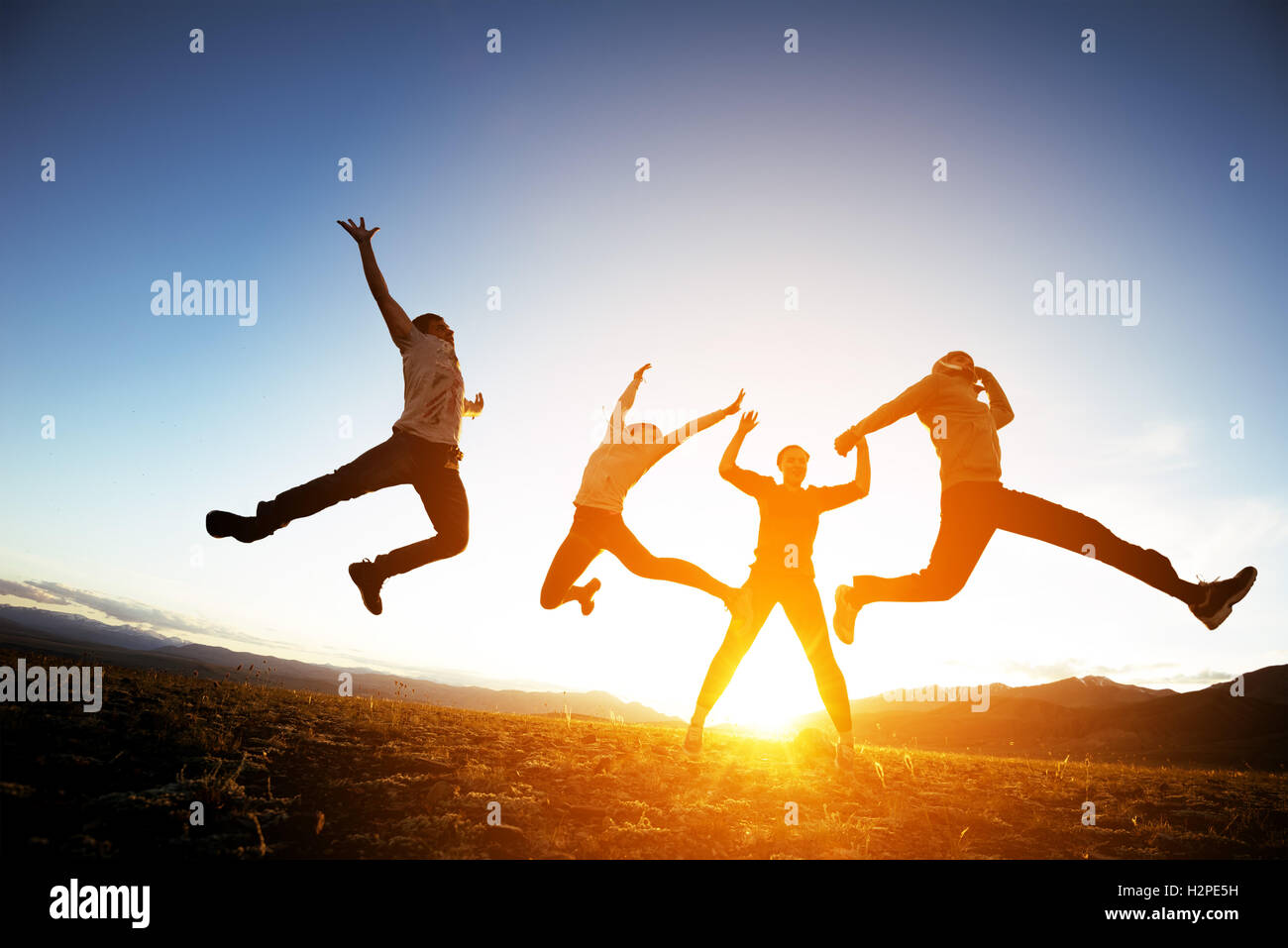 Group of friends having fun jumps on sunset and mountains Stock Photo