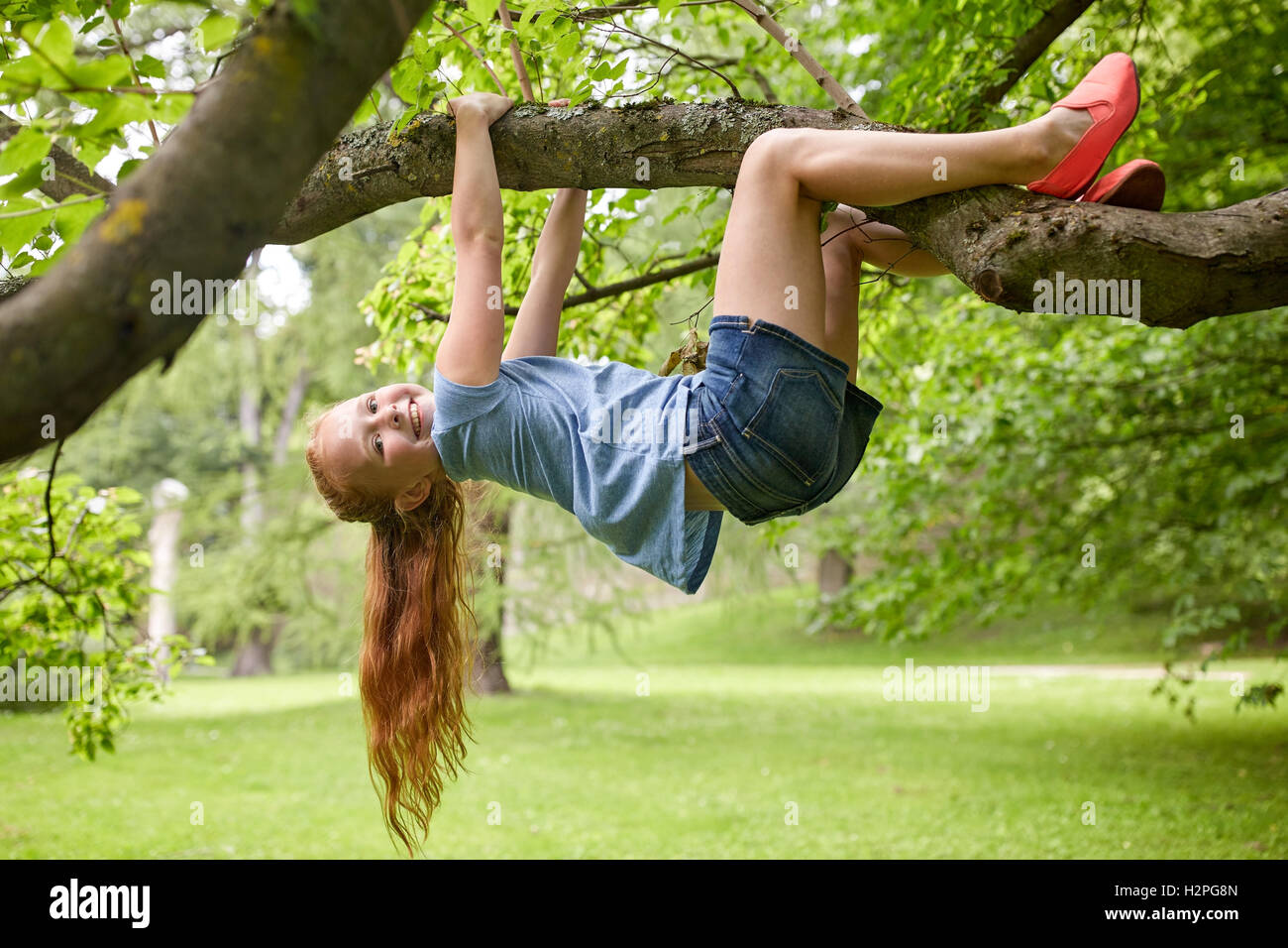 happy little girl hanging on tree in summer park Stock Photo