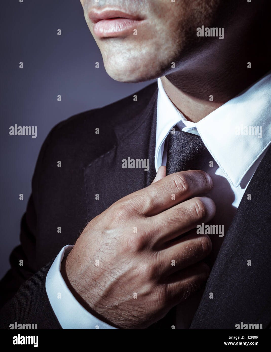 Closeup photo of a serious businessman wearing stylish black suit and tie over dark background, face part, mens wear fashion Stock Photo
