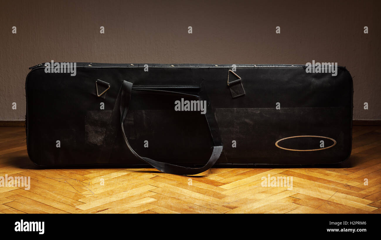 Old bass guitar suitcase, on parquet in front of a white wall Stock