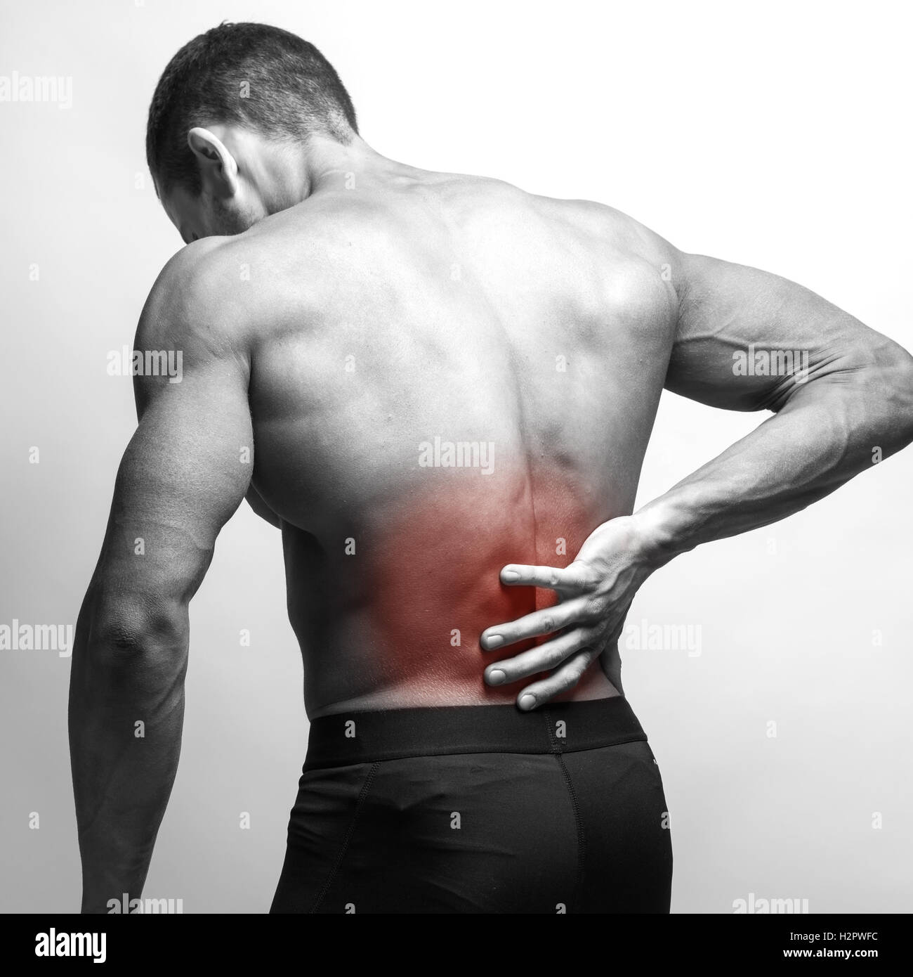 Male athlete with pain in his lower back, isolated in grey. Red spot