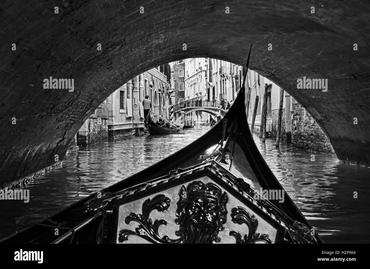 black white view from inside gondola in Venice passing under endless city bridges on busy tourist waterway Stock Photo