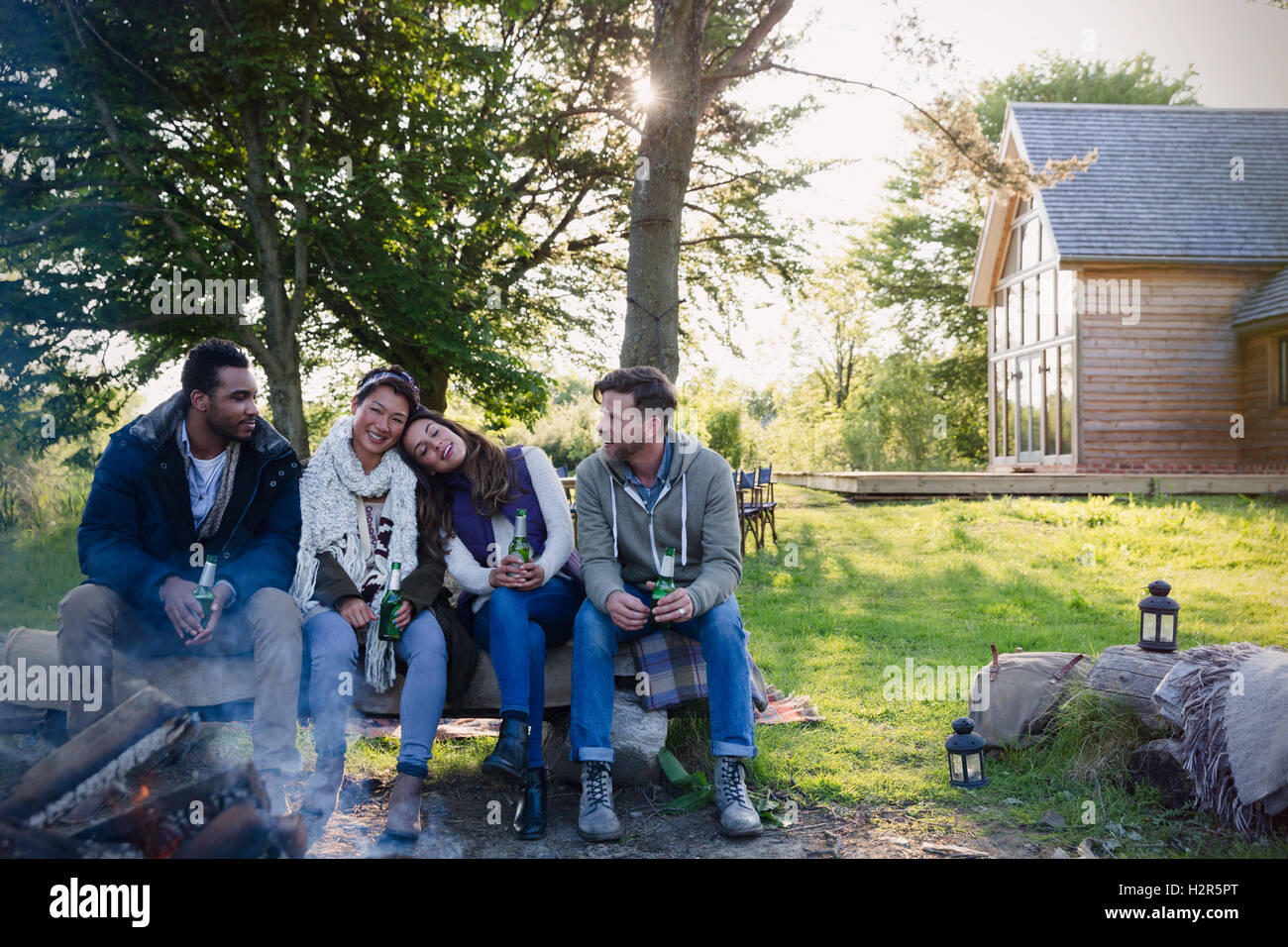 Friends drinking beer relaxing at campfire outside cabin Stock Photo