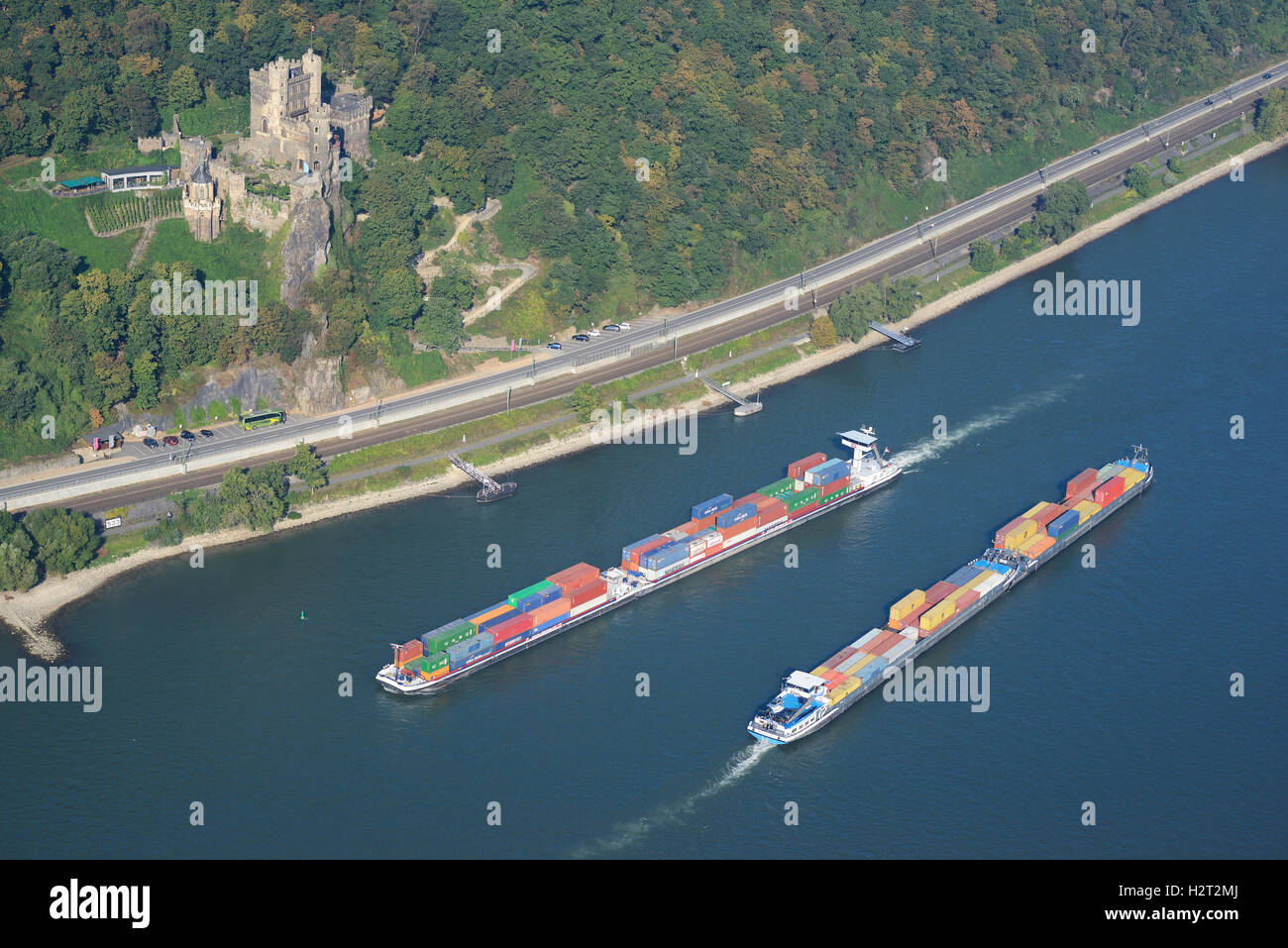 AERIAL VIEW. Container carriers on the heavily traveled Rhine River. Rheinstein Castle, Trechtingshausen, Rhineland-Palatinate, Germany. Stock Photo