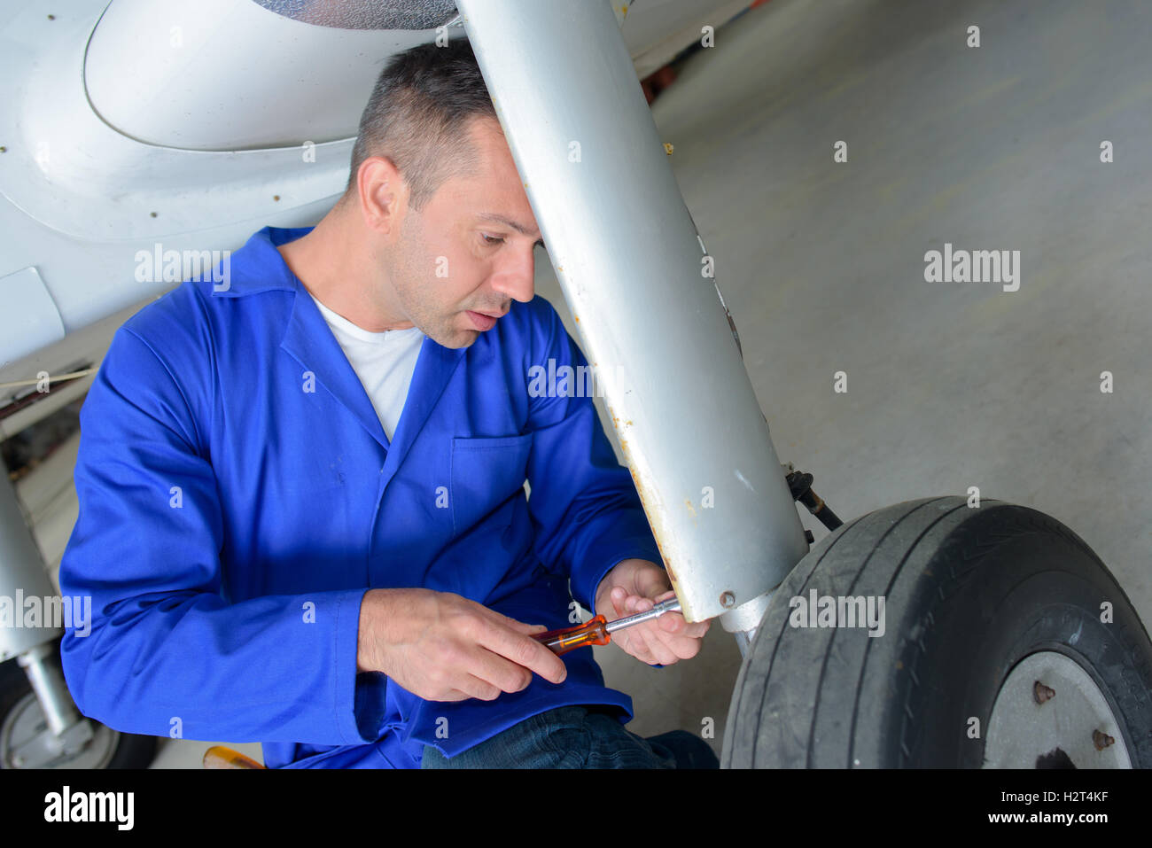 Mechanic with screwdriver working on aircraft landing gear Stock Photo