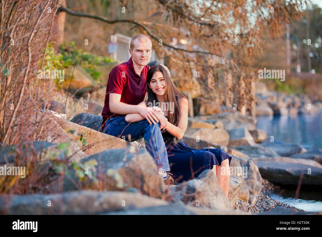 Young interracial couple sitting together on rocky shoreline by Stock Photo
