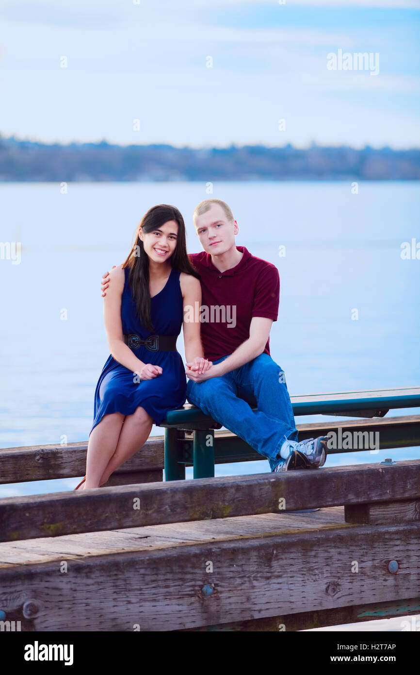 Young interracial couple sitting together on dock over lake Stock Photo
