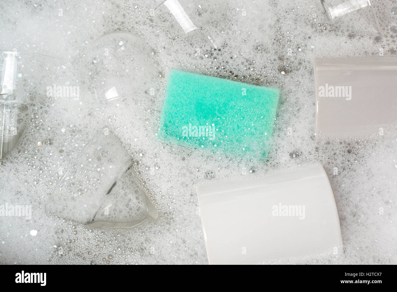 Glasses and cups in a sink full of soapy water with a washing uo sponge