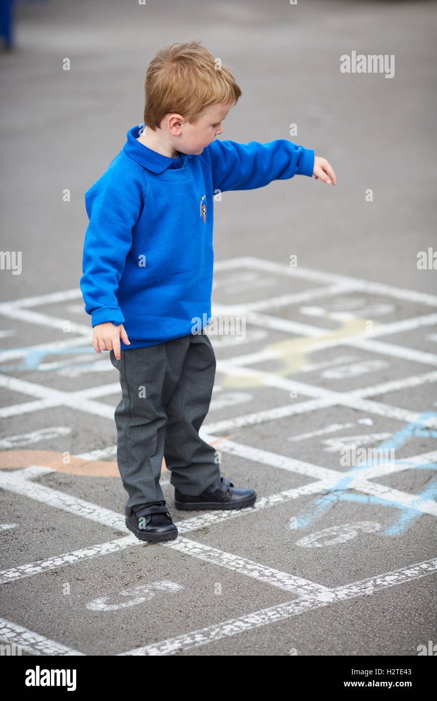 School boy child playground games  playing traditional chalk painted game snakes ladders uniform blue smart toddler Education ed Stock Photo