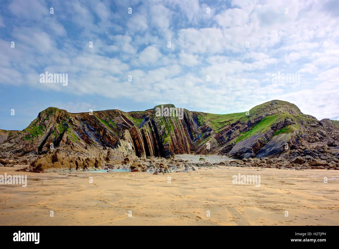 Detail of geological layers in coastal cliffs near Bude, England. The landscape features yellow sand, grass, rock and blue sky. Stock Photo