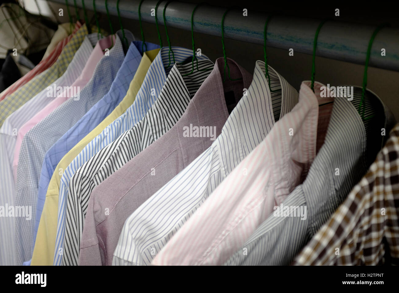 Row of dress shirts hanging on hangers in closet choice of clothing Stock Photo