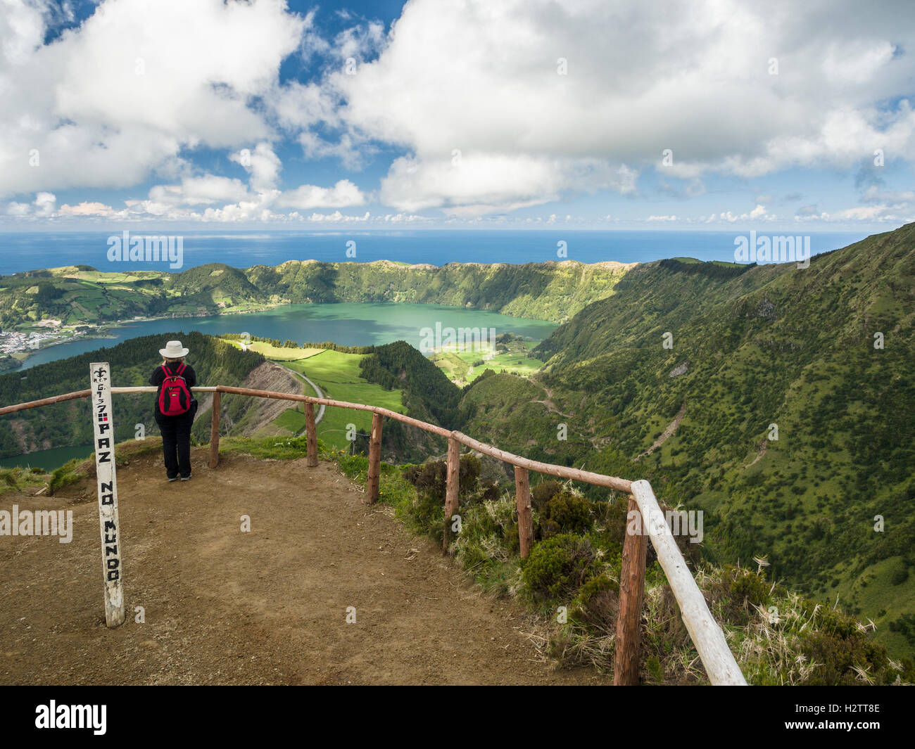Photographing Sete Cidades from Above. A woman at the end of the path pauses to photograph the awe inspiring landscape below. Stock Photo