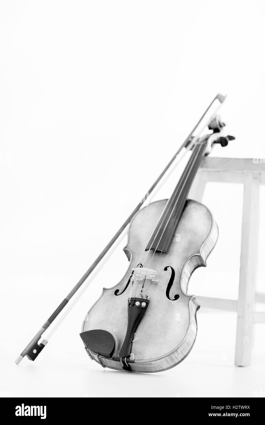 Black and White photograph of an Old Violin leaned by a stool on a white background Stock Photo