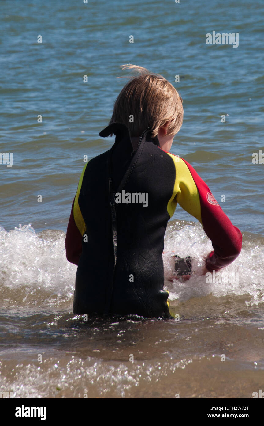 boy in wetsuit taking pictures of waves with small action camera Stock