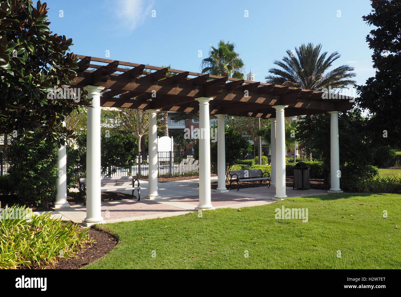 outdoor pavilion with a wood roof and columns.  There are benches under the pavilion and it is surrounded by lush vegitation Stock Photo
