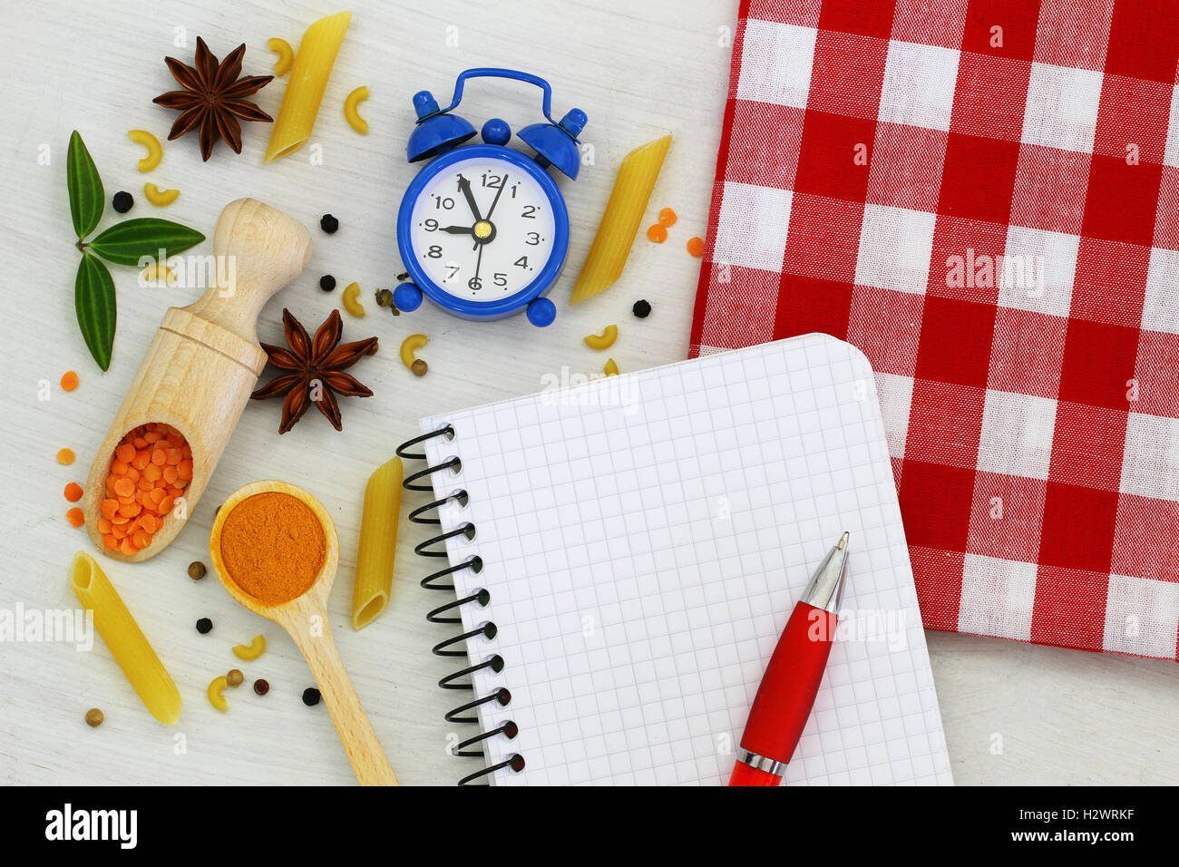Empty notebook with pen, miniature clock and different ingredients spread around it Stock Photo