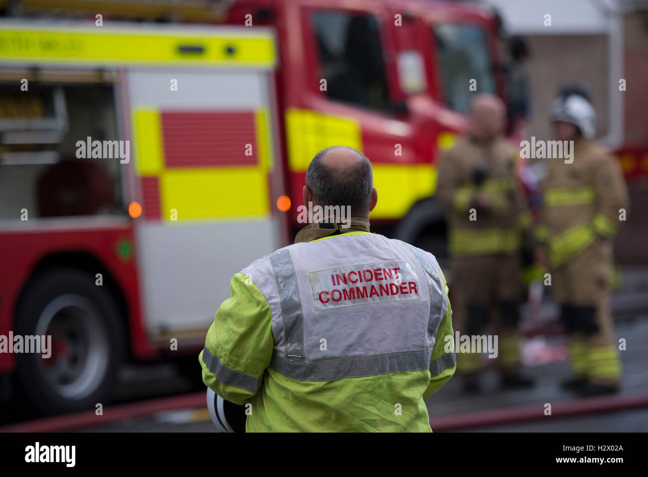 An incident commander looks on at the scene of a fire attended by firemen and a fire engine. Stock Photo