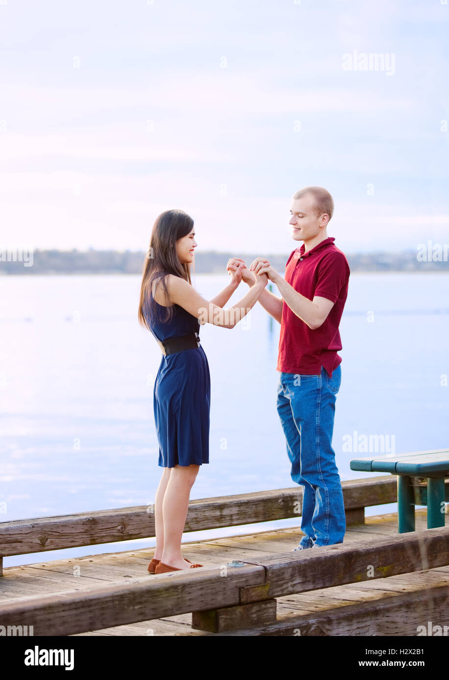 Young interracial couple holding hands standing on dock over lak Stock Photo