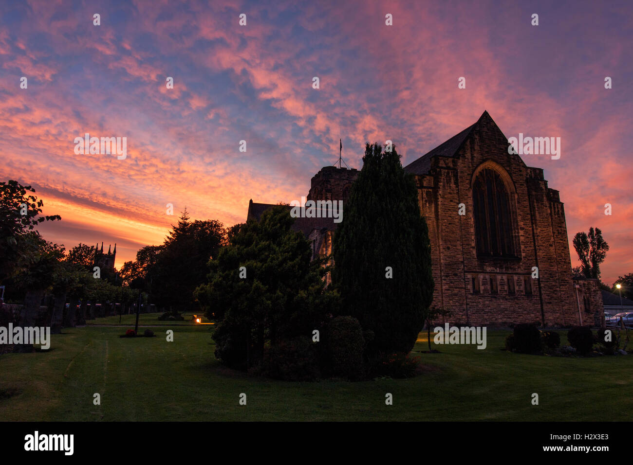Beautiful serene sunset over a church, with pinks and orange clouds in a perfect blue sky, surrounded by trees and grass. Stock Photo