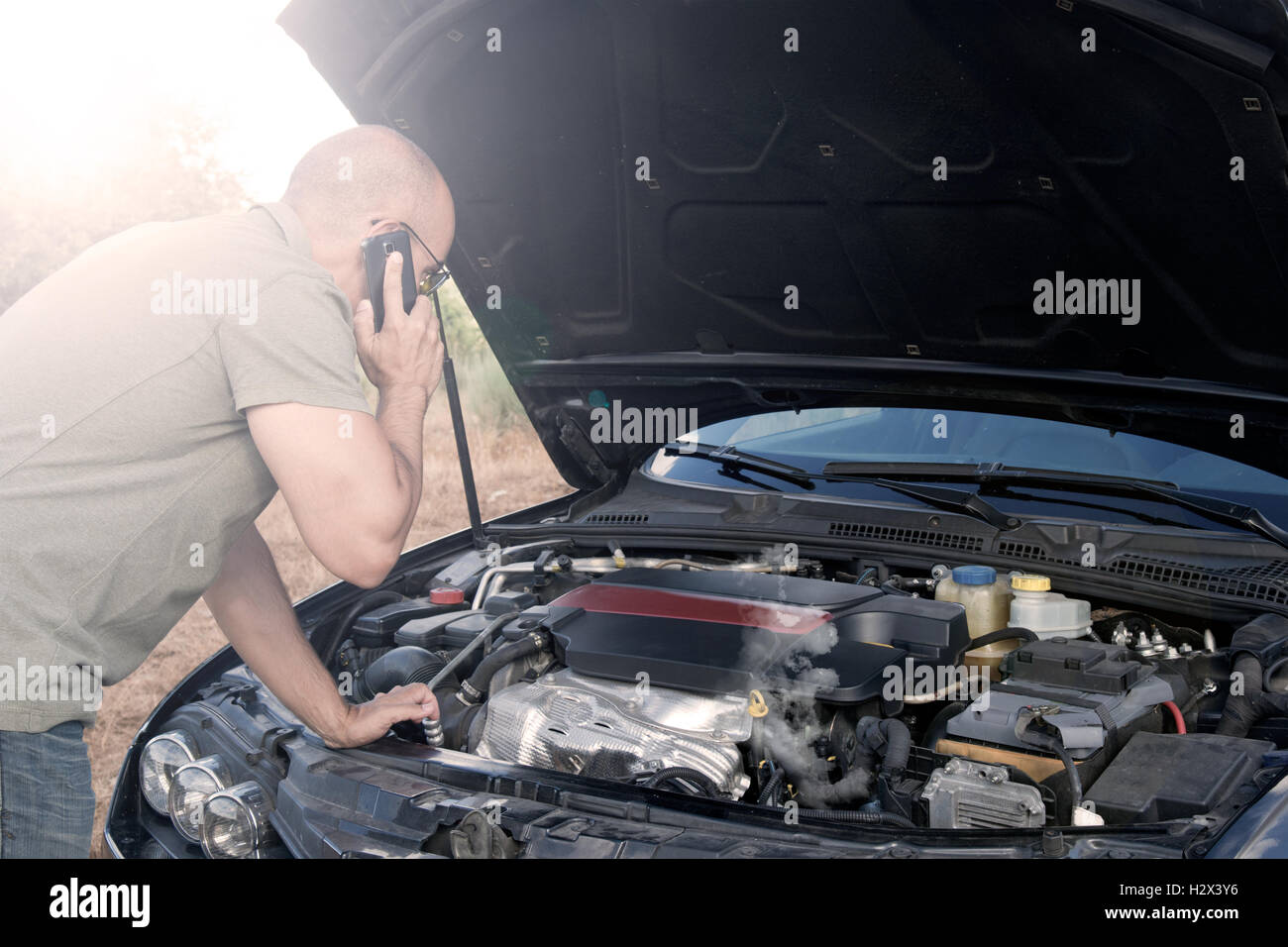 Close up of a broken down car, engine open and smoking, in a rural area and the driver looking at the engine Stock Photo