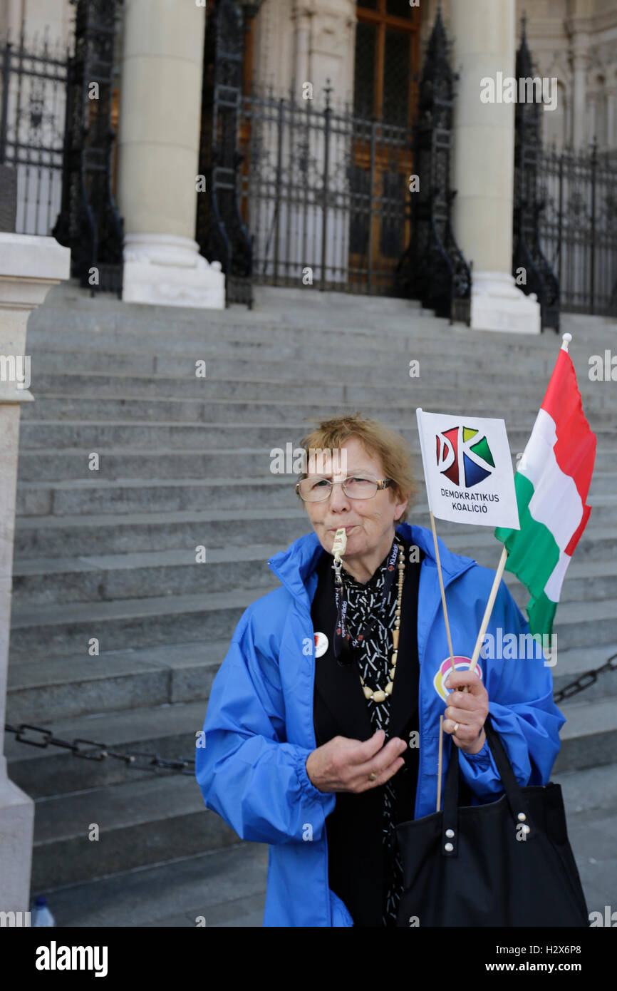 A woman holds a Democratic Coalition placard, a Hungarian flag and blows a whistle, to disturb the neighbouring right wing demonstration. The last day ahead of the Hungarian migrant quota referendum saw two protests outside the Hungarian Parliament building. On the one side of the square protested members of the Democratic Coalition, including their leader, the former Prime Minister of Hungary Ferenc Gyurcsany, for a boycott of the referendum. On the other side of the square called supporters of the right wing Jobbik for a ‘No' vote. the Right wing protest was also attended by members of the m Stock Photo