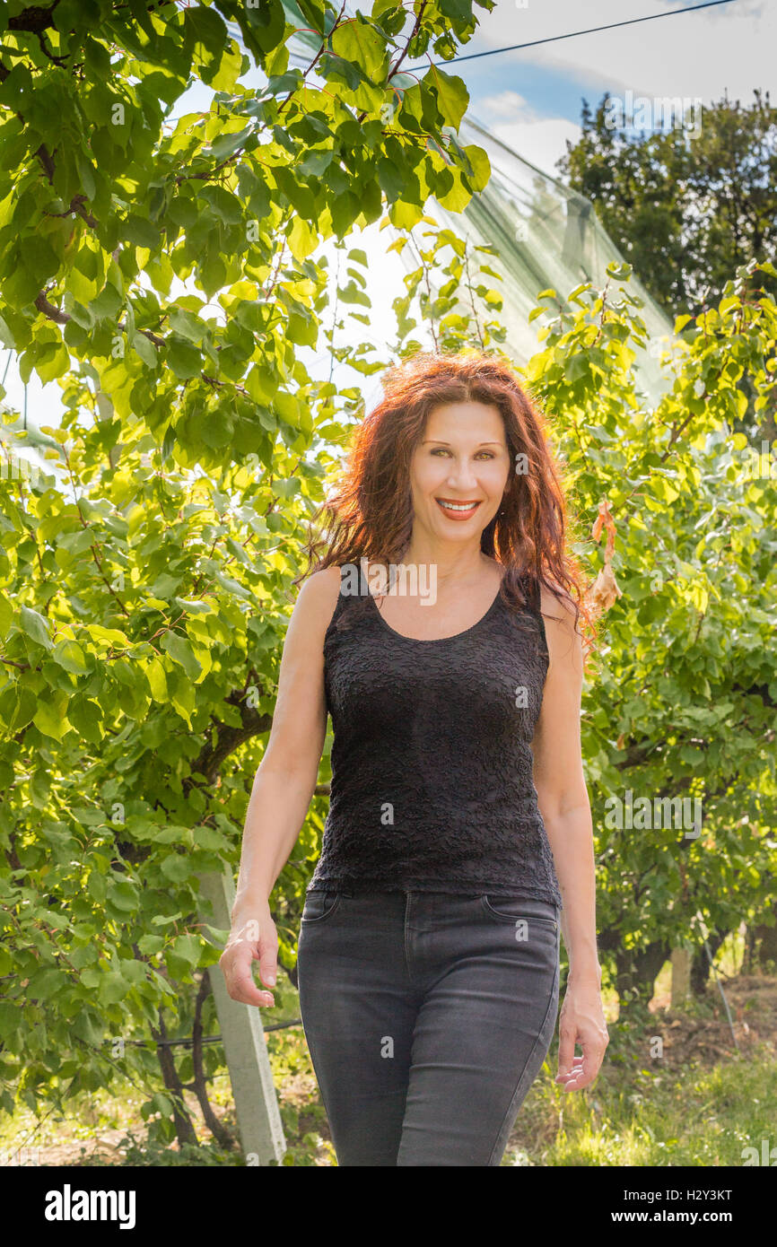 nice red woman enjoying nature of a countryside while walking in the apple orchard in Autumn season Stock Photo