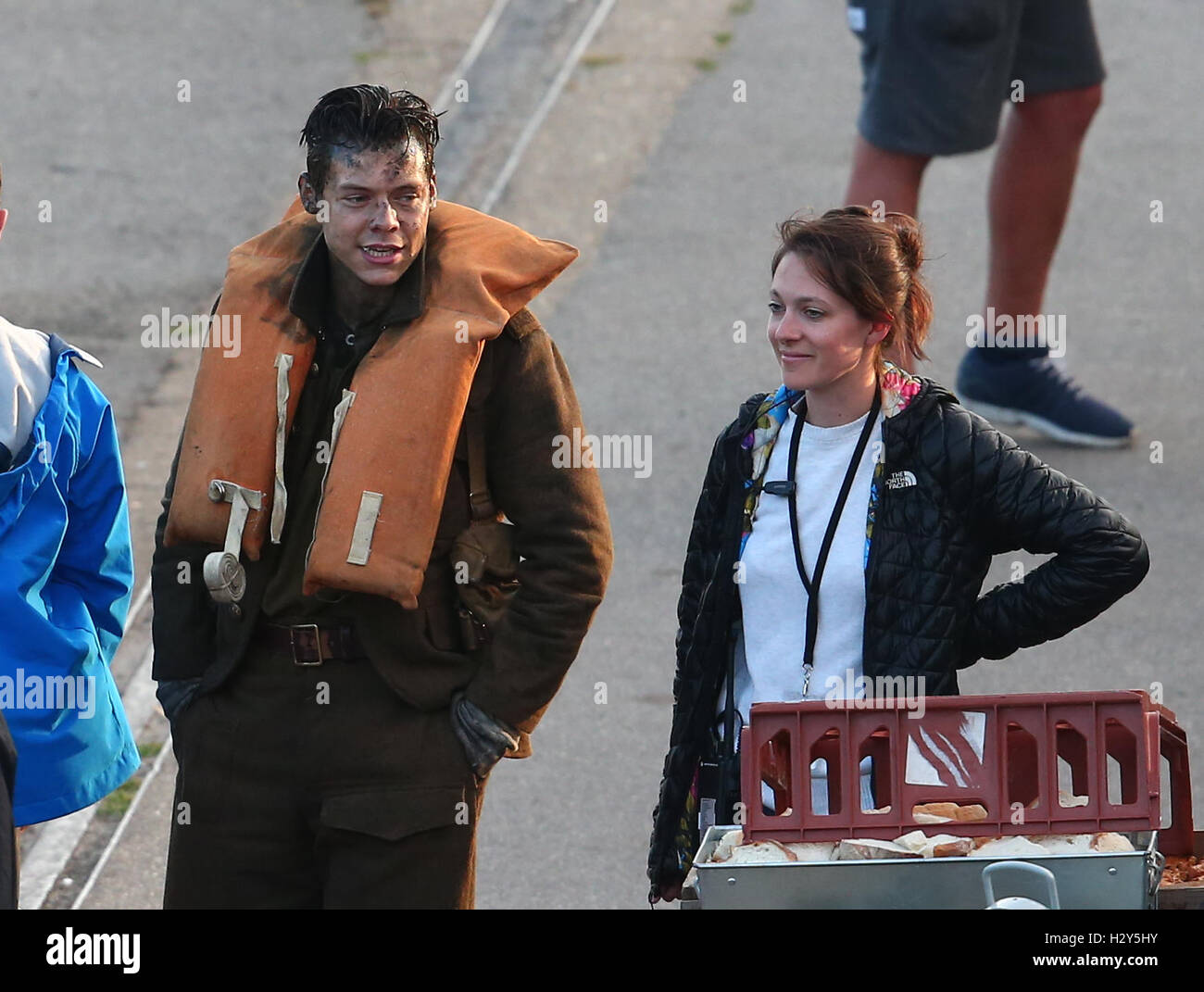 Harry Styles struggles putting on his life vest, and then chats with a female production crew member.  Featuring: Harry Styles Where: Weymouth, United Kingdom When: 28 Jul 2016 Stock Photo