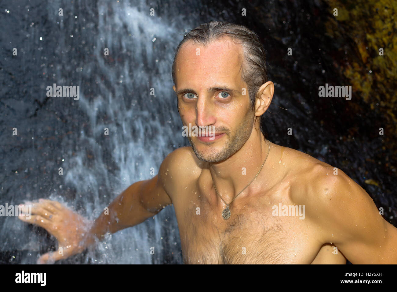 a man taking a relaxing shower under a waterfall outside Stock Photo