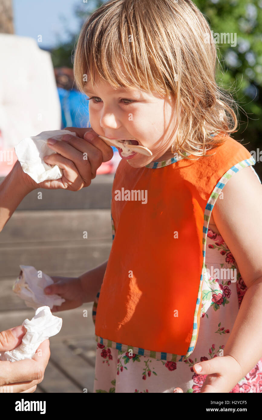 portrait of three years old blonde child with orange bib eating