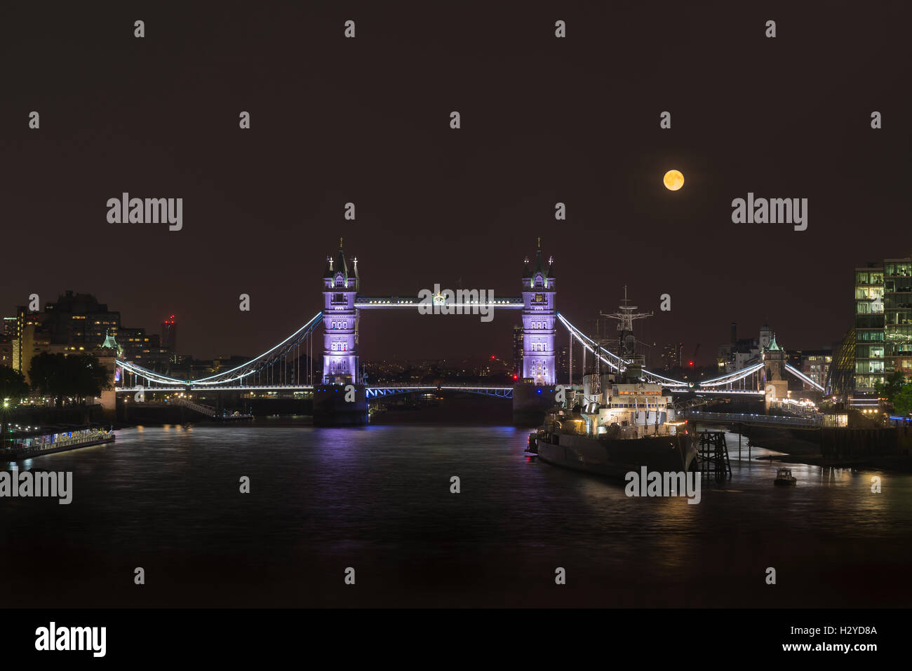 Full moon rising over the illuminated Tower Bridge, the HMS Belfast museum ship and the River Thames, London, UK Stock Photo