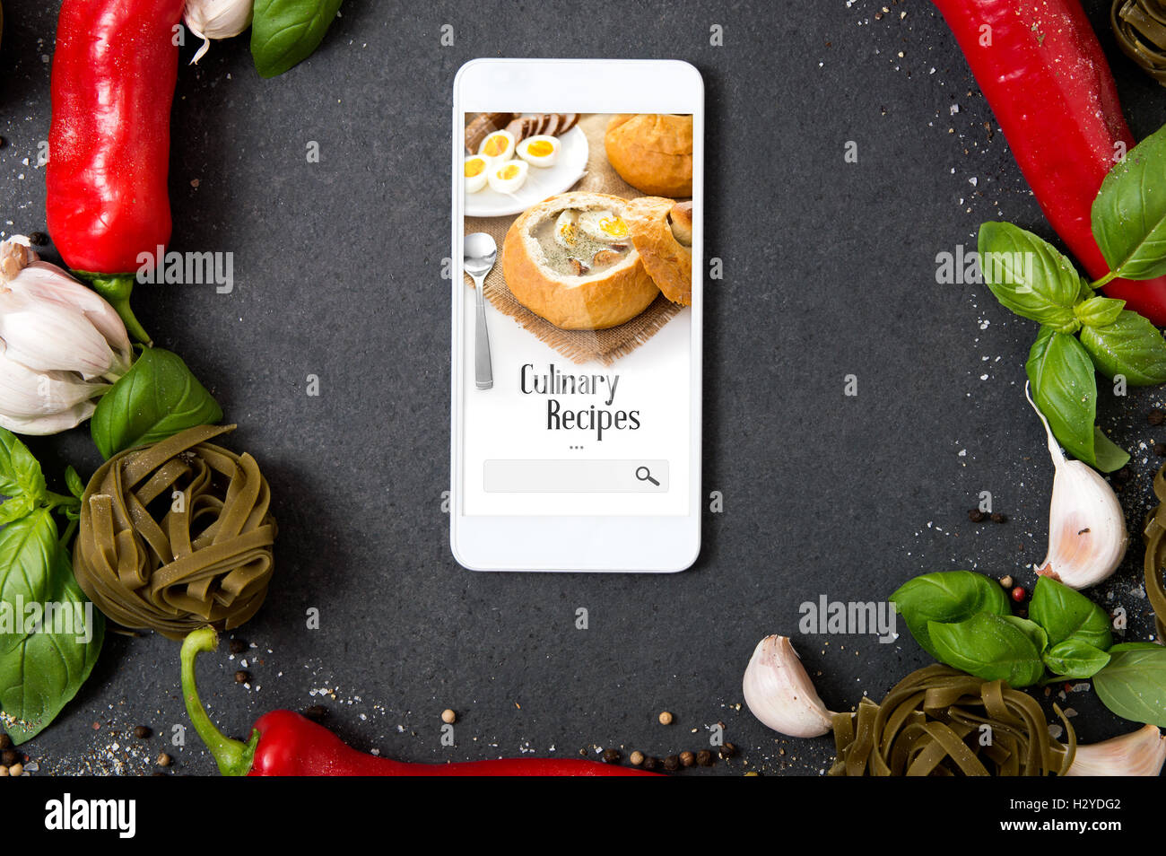 Smartphone with culinary recipes application lying on stone countertop and surrounded by fresh herbs and hot spices Stock Photo