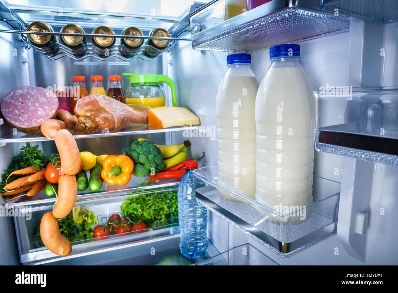 https://c8.alamy.com/comp/H2YDXT/open-refrigerator-filled-with-food-focus-on-bottles-of-milk-in-the-H2YDXT.jpg