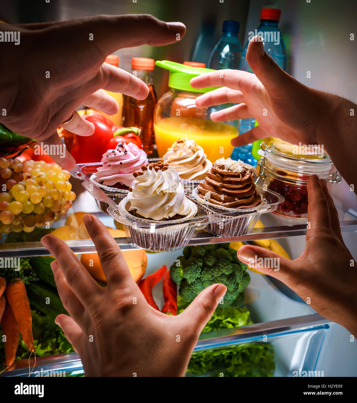Human hands reaching for sweet cake at night in the open refrigerator Stock Photo