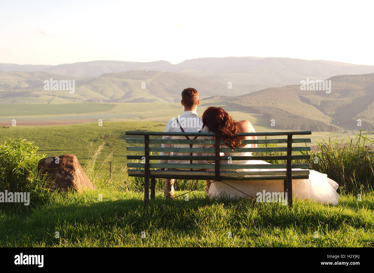 African bride and groom on bench with landscape Stock Photo