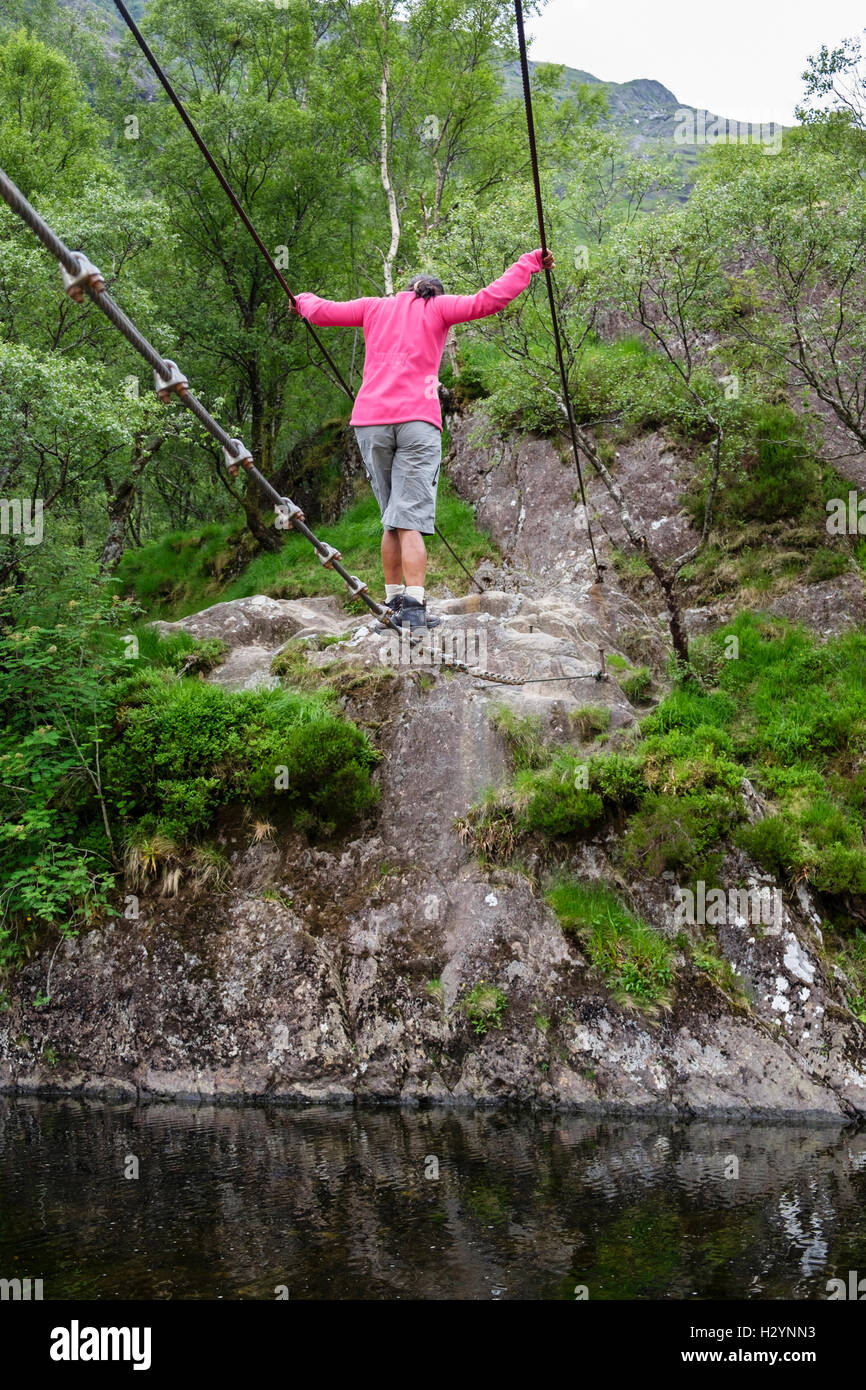A woman walking across Steall wire rope bridge crossing River Nevis