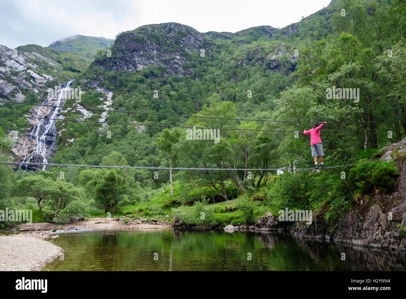 woman walking across steall wire bridge over water of nevis river