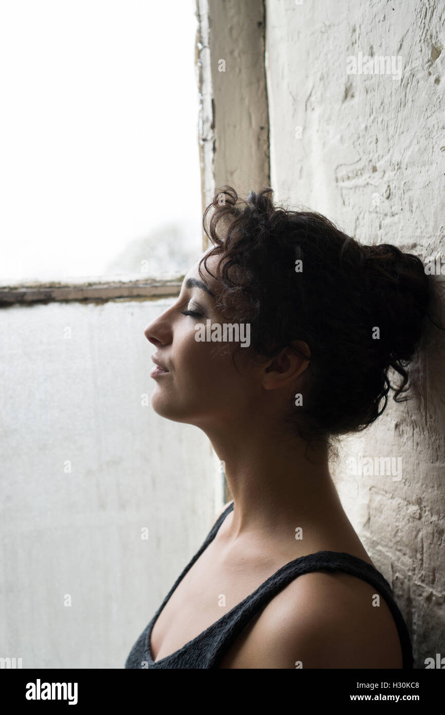 Woman leaning against the wall by the window eyes closed Stock Photo