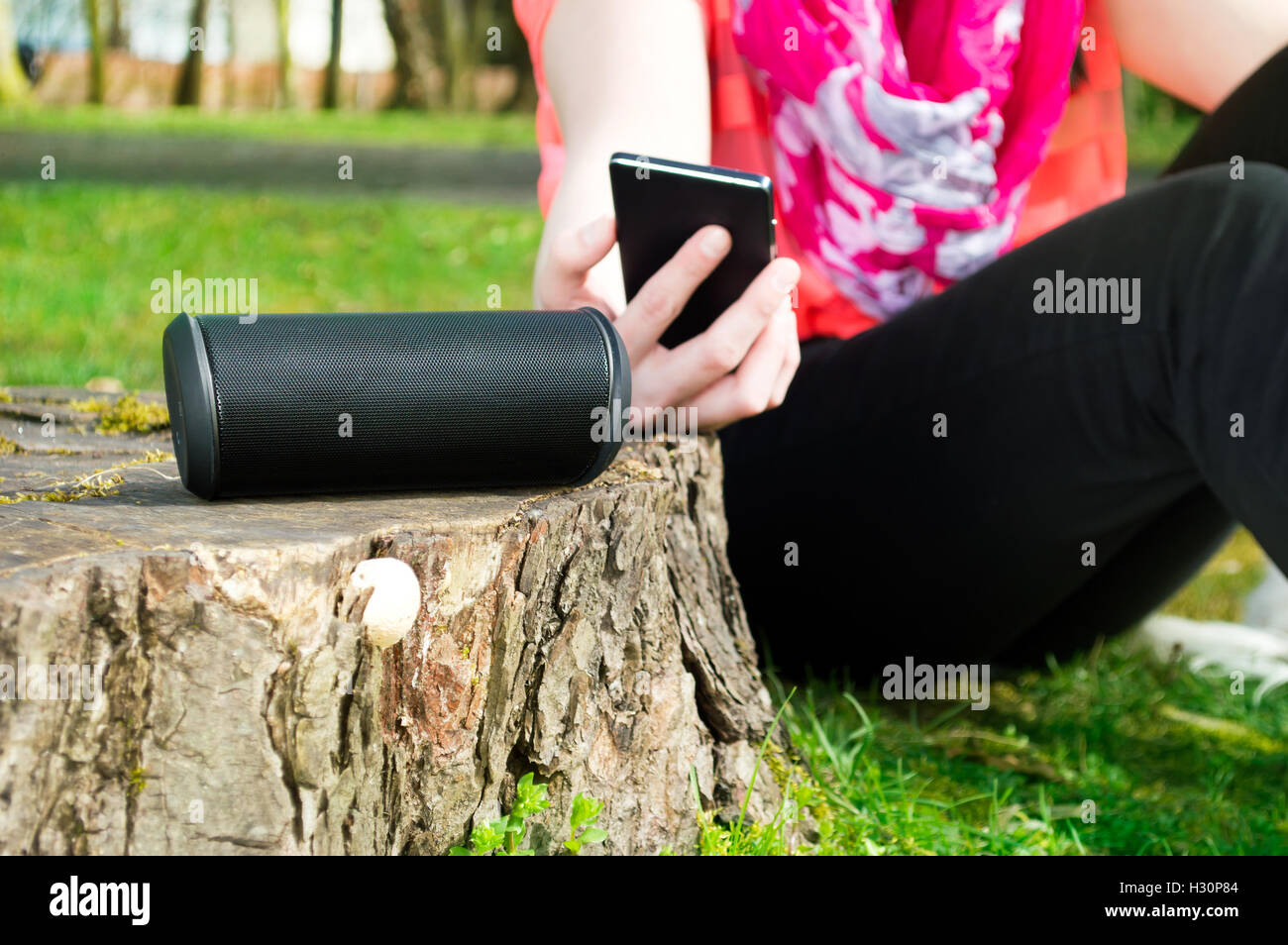 Woman is connecting her smartphone with wireless speaker while being outdoor. Stock Photo