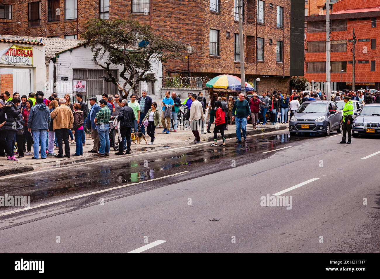 Bogota, Colombia - October 02, 2016: Voters queuing up to enter a polling station on Carrera 9, in the Andean capital city of Bogota, in the South American country of Colombia, to vote on the historic Peace Referendum. A policeman has stopped the traffic to enable voters to cross the road. Photo shot in the afternoon sunlight. Horizontal Format. Stock Photo