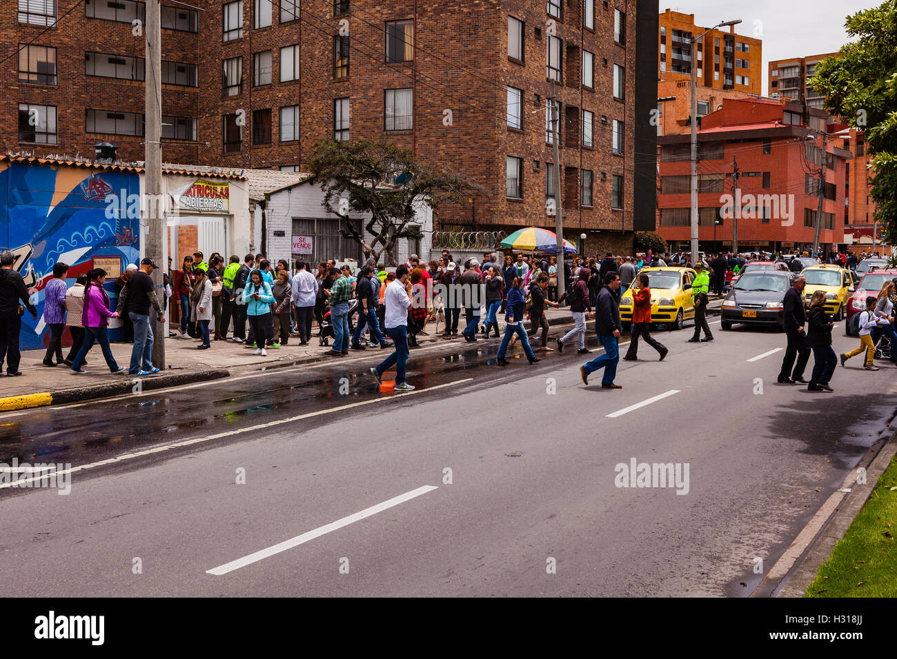 Bogota, Colombia - October 02, 2016: Voters queue up to enter a polling station on Carrera 9, in the Andean capital city of Bogota, in the South American country of Colombia, to vote on the historic Plebiscite on the peace process with FARC. To the left behind the people is part of a mural painted in the bright colours of Latin America, dedicated to the Peace Process. A policeman has stopped the traffic to help people cross the road safely. Stock Photo