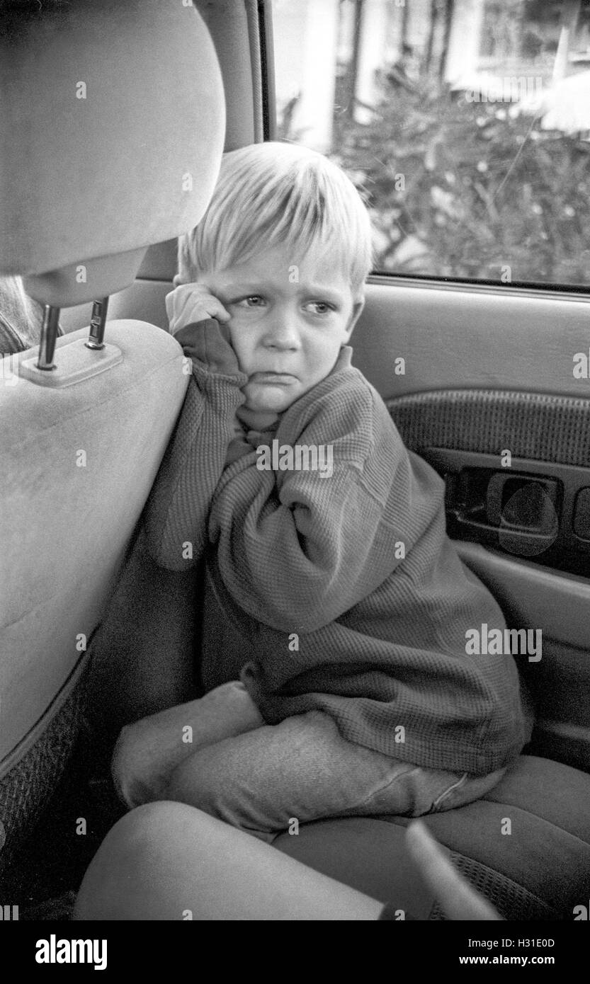 An angry, pouting toddler boy frowns in the back seat of his parent's car in Corona, CA. MODEL RELEASE Stock Photo