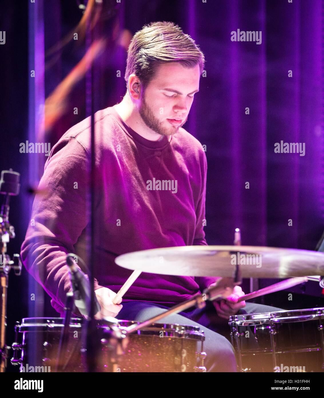 a drummer on stage with his eyes closed playing to the music with light shining all around. Stock Photo
