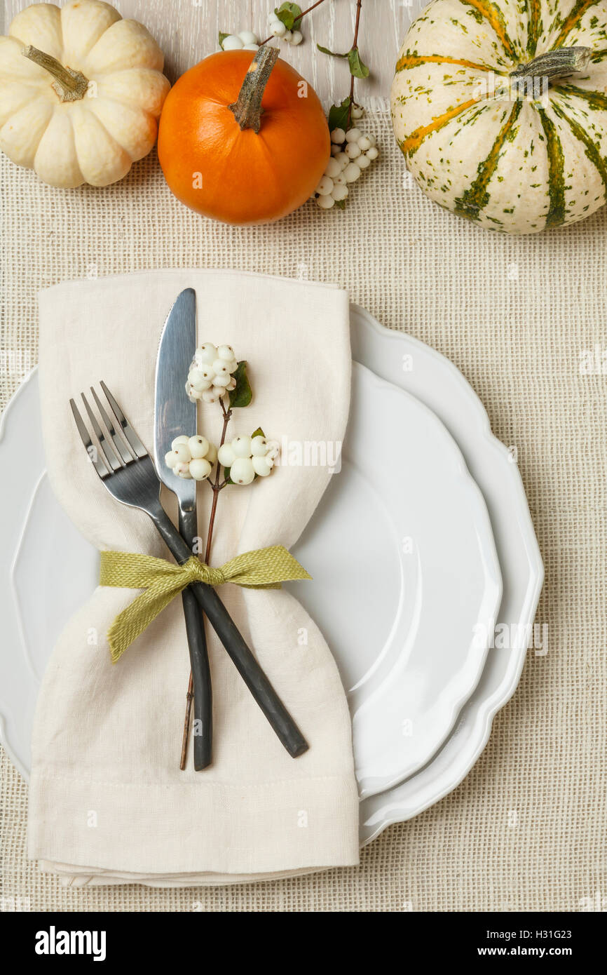 Fall autumn festive Thanksgiving dinner table place setting with miniature pumpkins, plate, fork, knife and napkin on burlap background Stock Photo