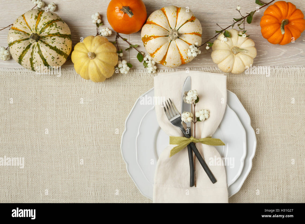 Fall autumn festive Thanksgiving dinner table place setting with miniature pumpkins, plate, fork, knife and napkin on burlap background Stock Photo