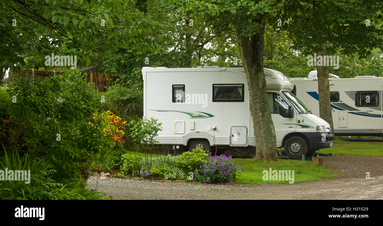 Modern motorhome / mobile home among shading trees, verdant lawns, and colourful gardens at Ravenglass caravan park, Cumbria England Stock Photo