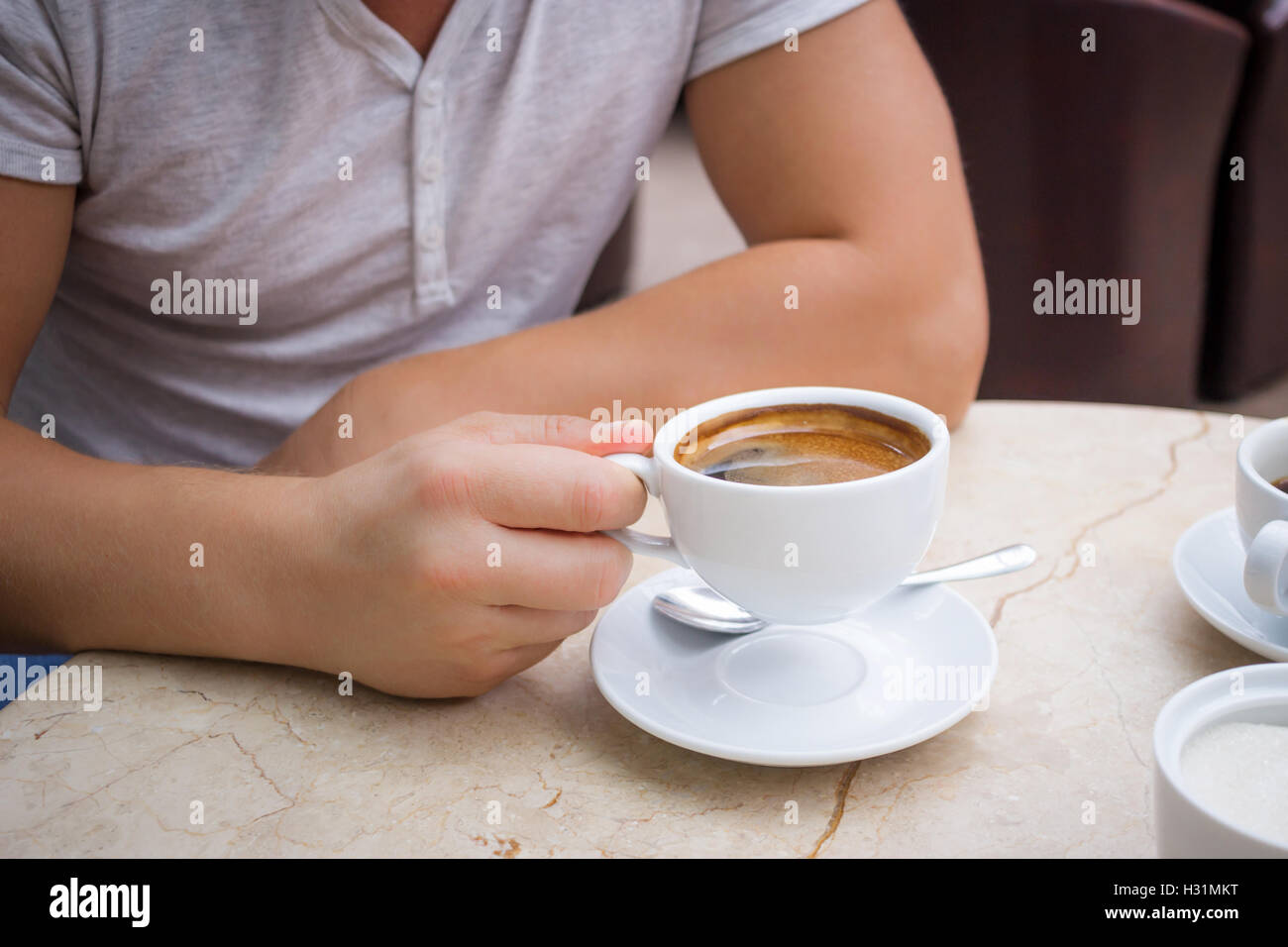 Man at marble table holds a cup of americano coffee in his hand Stock Photo