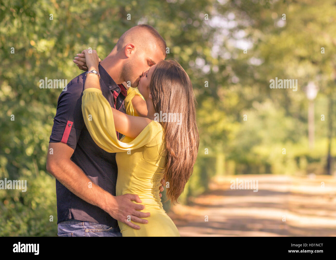 young adult 20s couple kissing outdoors sunny day profile side view Stock Photo